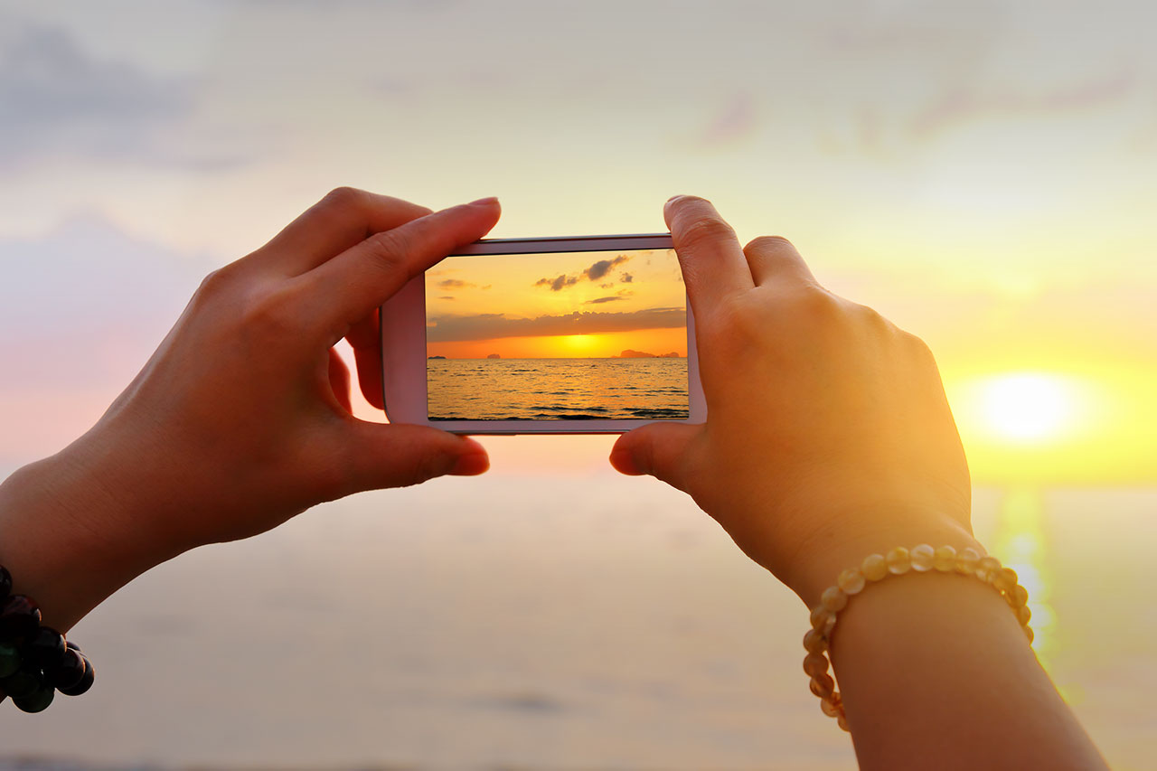 Hands holding iPhone taking photo of sunset